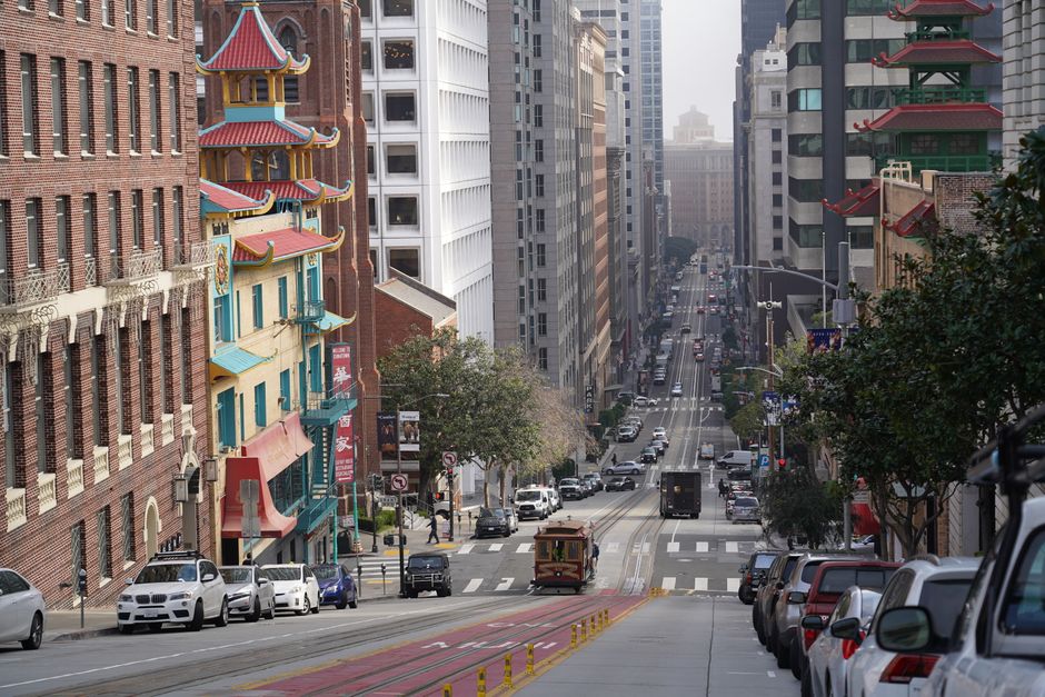 A classic San Francisco cable car ascending a steep hill, with the city skyline visible in the background, representing iconic car-free transport.