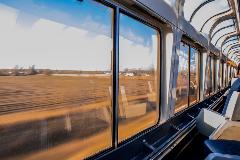 A person enjoying a panoramic view of the Swiss Alps from inside a scenic train's large window, with snow-capped peaks and a winding river.