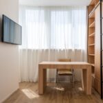 A neatly organized small home office setup in a cozy apartment, featuring a wall-mounted monitor and floating shelves maximizing vertical space.