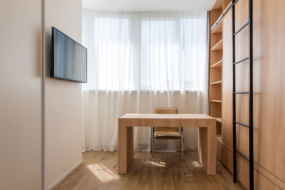 A neatly organized small home office setup in a cozy apartment, featuring a wall-mounted monitor and floating shelves maximizing vertical space.