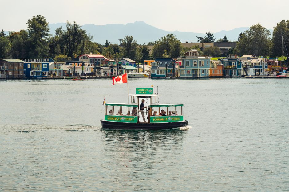 A small boat with passengers cruising past city skyscrapers and mountains in Vancouver's inner harbor.