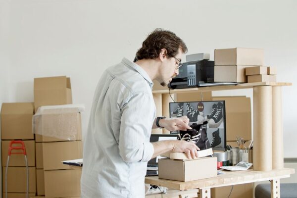A small business owner looking thoughtfully at different printer boxes in a store aisle, weighing options for occasional use.