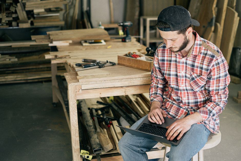 A small business owner looking thoughtfully at an old silver laptop, considering its future.