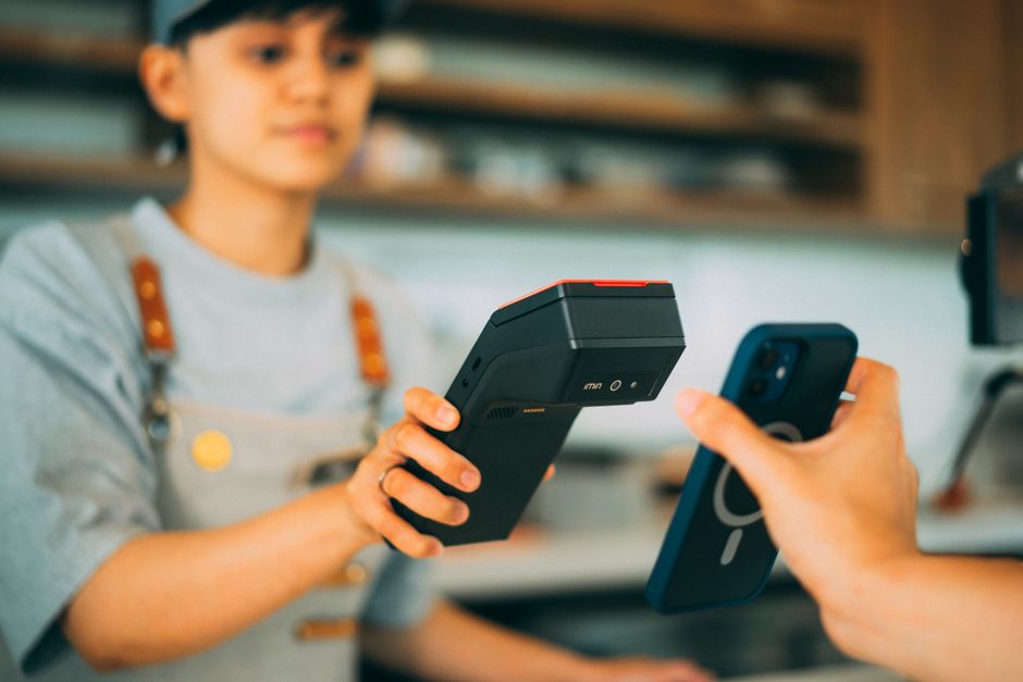 A close-up of a hand holding a smartphone to a payment terminal, illustrating contactless NFC payment.