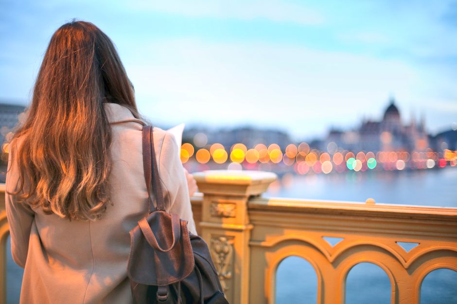 A solo female traveler smiles while browsing fresh produce at a vibrant European market, her small backpack beside her.