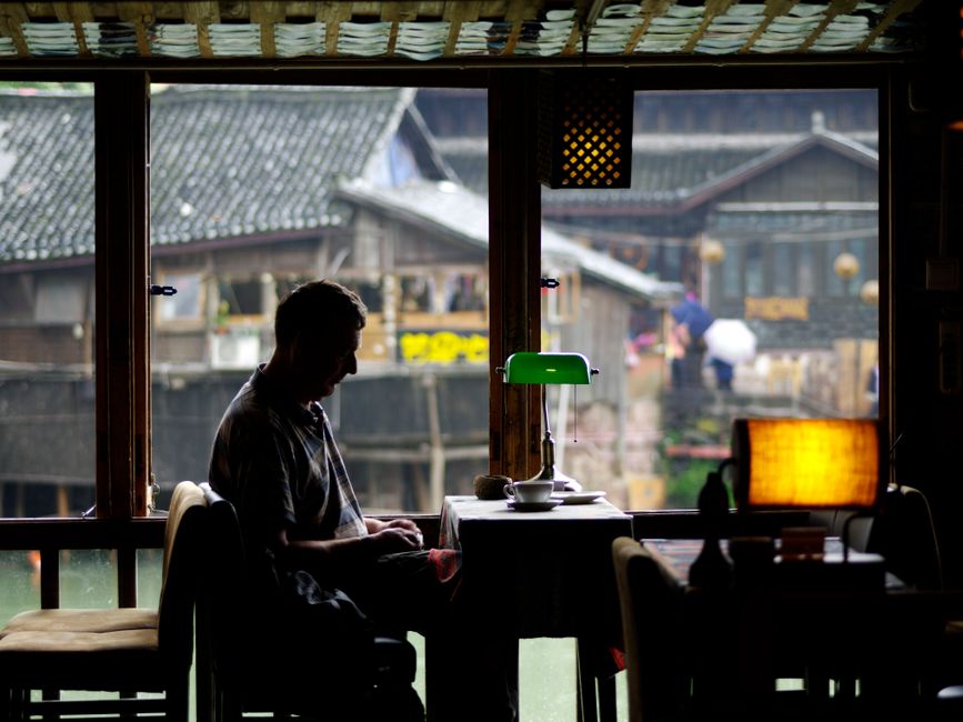 A solo woman traveler sips coffee peacefully at an outdoor cafe, with a travel journal and phone on the table, indicating a relaxed morning.
