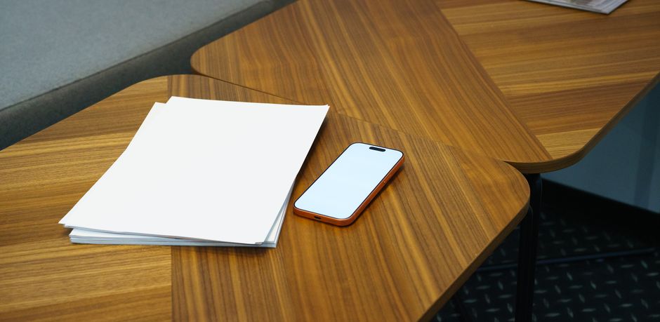 A stack of various refurbished smartphones, including Samsung and iPhone models, neatly arranged on a modern office desk.