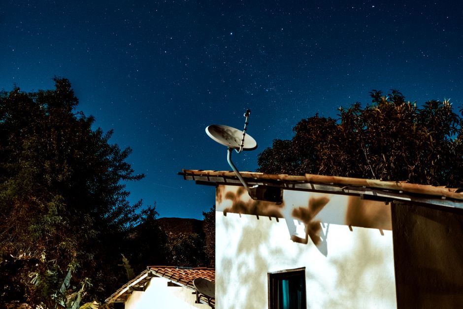 A Starlink satellite dish mounted on a pole in a remote, mountainous rural landscape, connecting isolated homes.