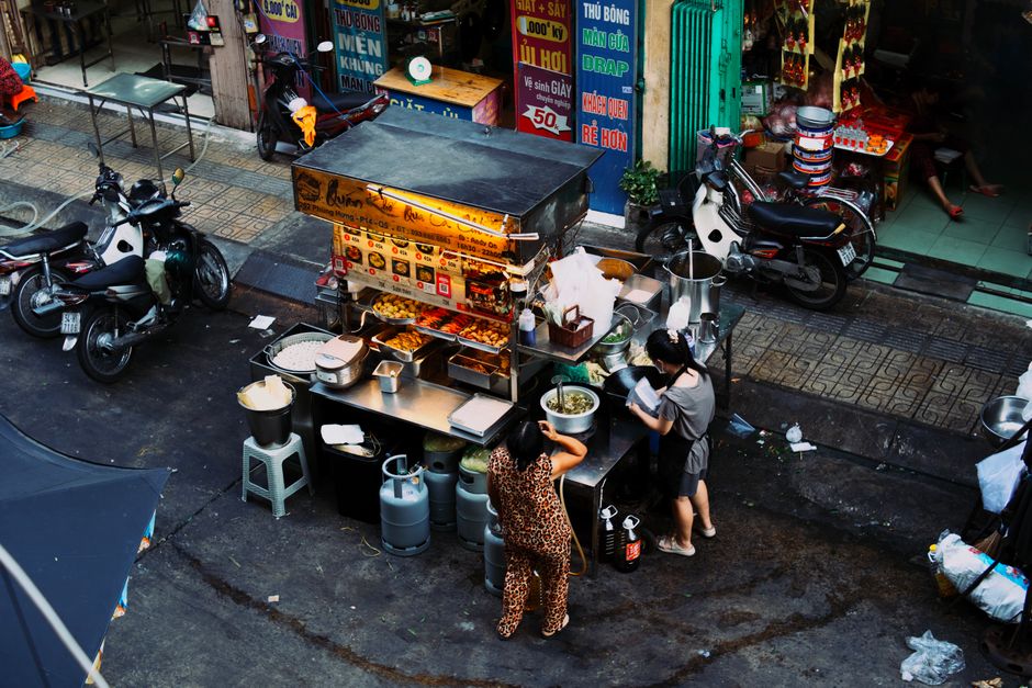 A local street food vendor in a market preparing fresh tacos or empanadas, with smoke rising and patrons waiting patiently.