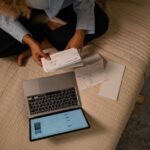Young person reviewing financial statements on a laptop with coffee, showing various recurring subscription charges.