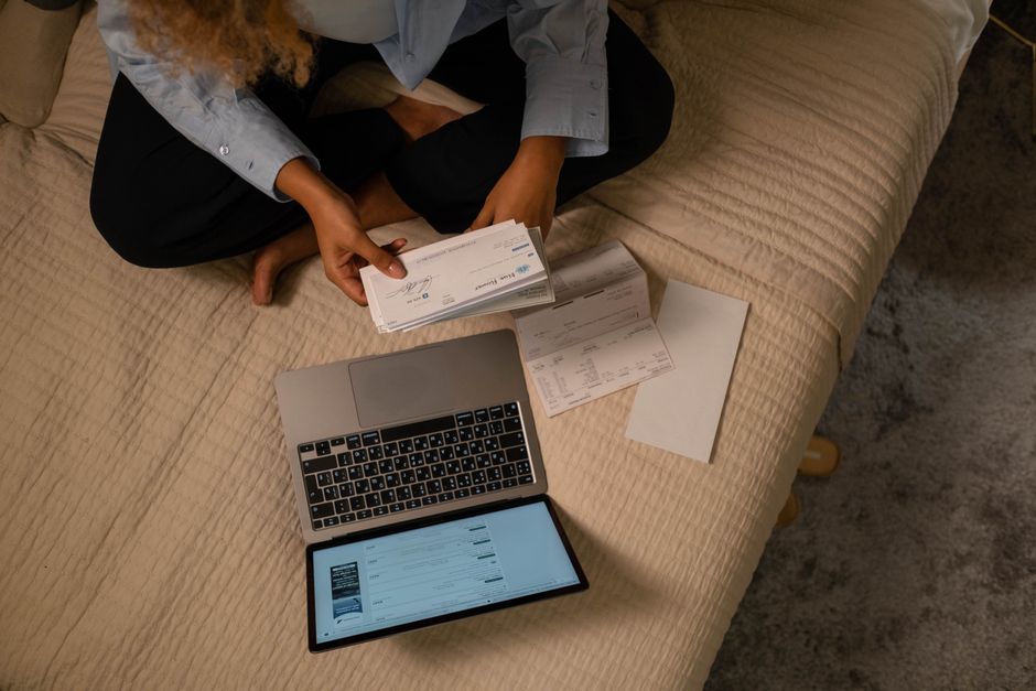 Young person reviewing financial statements on a laptop with coffee, showing various recurring subscription charges.