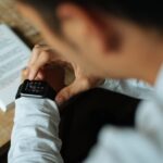 A student in a library checking discreet notifications on their smartwatch, a textbook open in front of them.