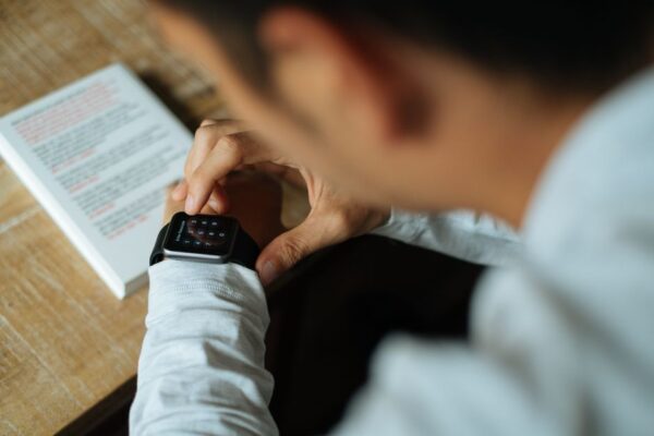 A student in a library checking discreet notifications on their smartwatch, a textbook open in front of them.