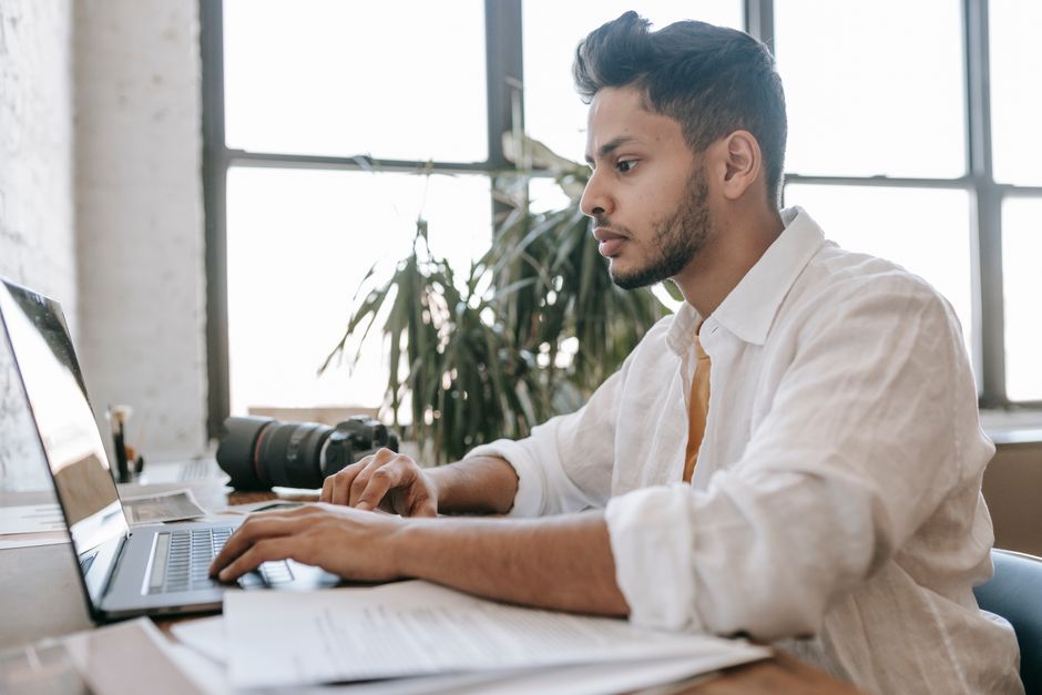 A student in a modern cafe intently reviewing and editing a resume displayed on a laptop, with notes and coffee beside them.