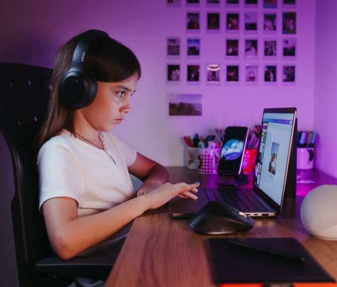 A person with a gaming laptop open on a desk, with textbooks and a notebook nearby, suggesting a balance of study and play.