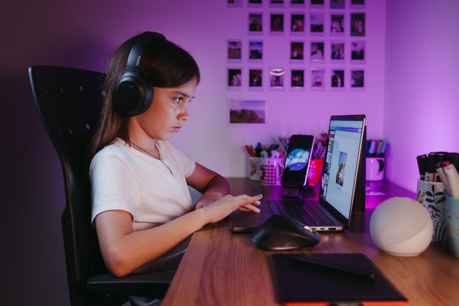 A person with a gaming laptop open on a desk, with textbooks and a notebook nearby, suggesting a balance of study and play.