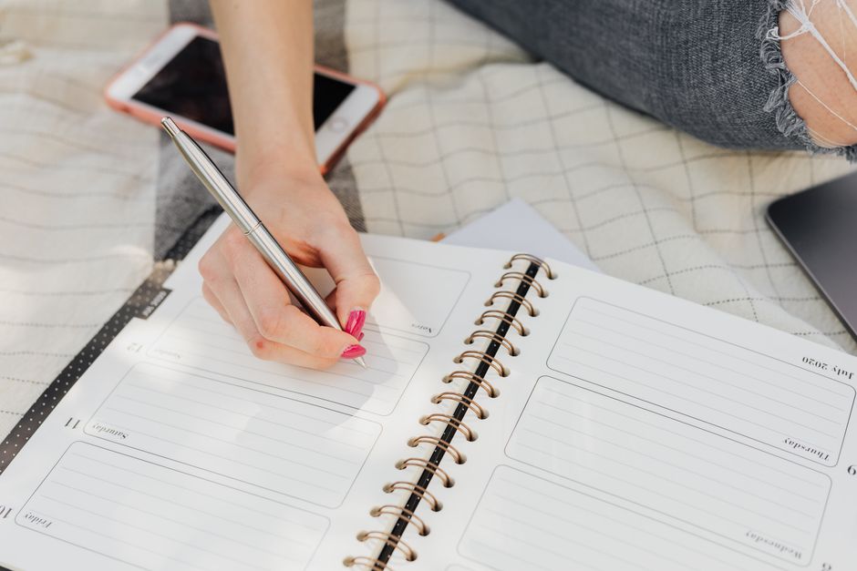 A student or young professional reviewing a physical planner and digital calendar, surrounded by a laptop and coffee.
