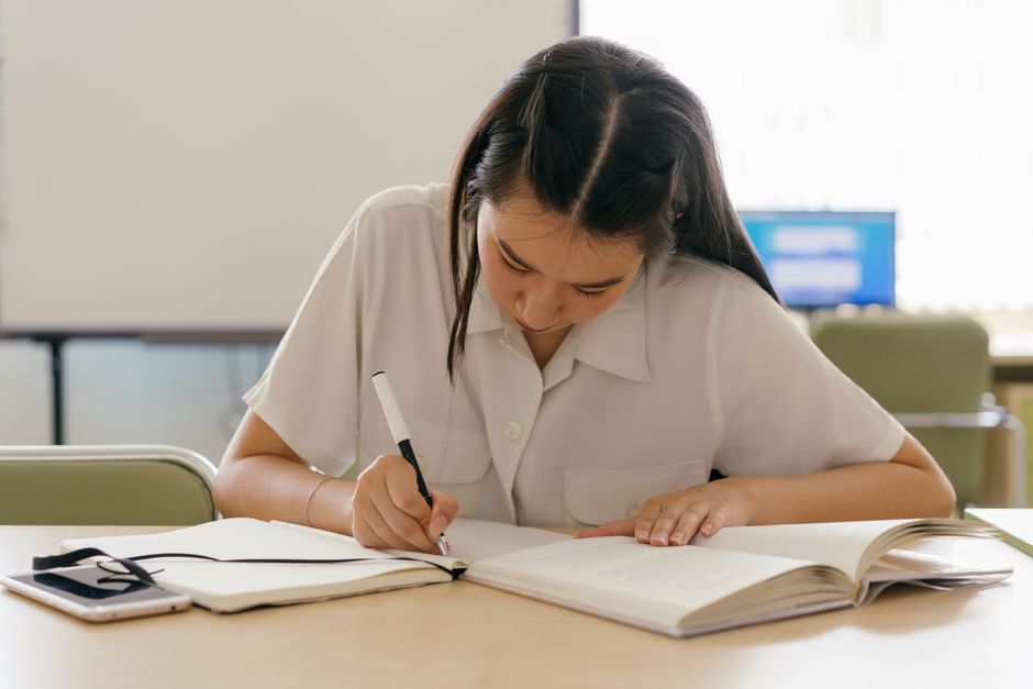 A student in a library or coffee shop, focused on their budget smartphone, possibly reading an e-book or collaborating on a document.