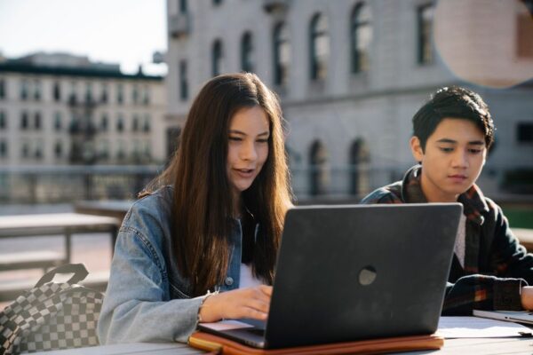 A student with glasses focused on a laptop screen, showing an AI chat interface, surrounded by open textbooks and notes.