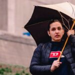 A stylish person in a trench coat walking through a rainy city street, protected from the elements.
