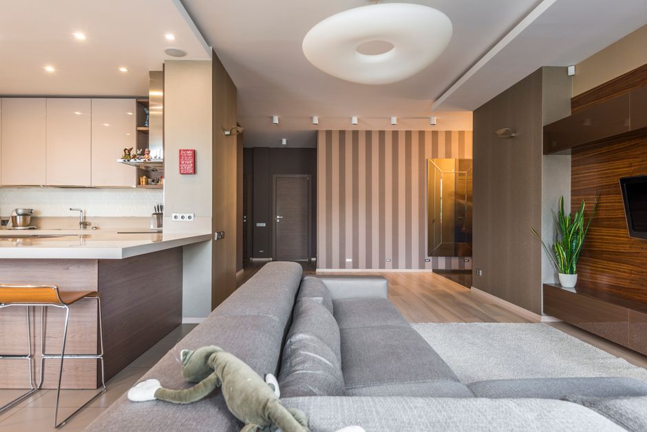 A stylish small living room featuring a sofa bed, a floating shelf with books, and a mirror reflecting the window, making the space appear larger.