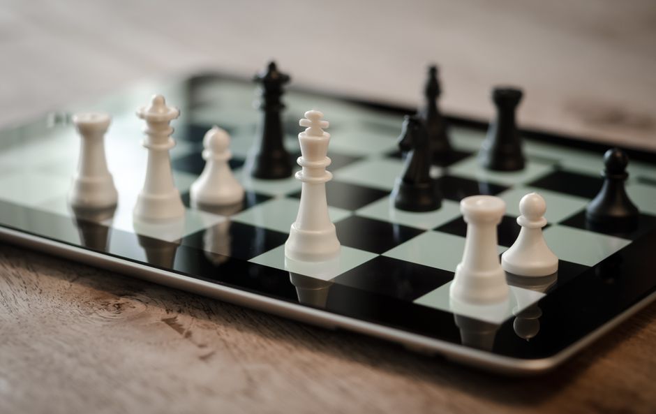 Close-up of a tablet screen displaying a digital board game, next to a cup of coffee on a table, suggesting a cozy, remote gaming session.