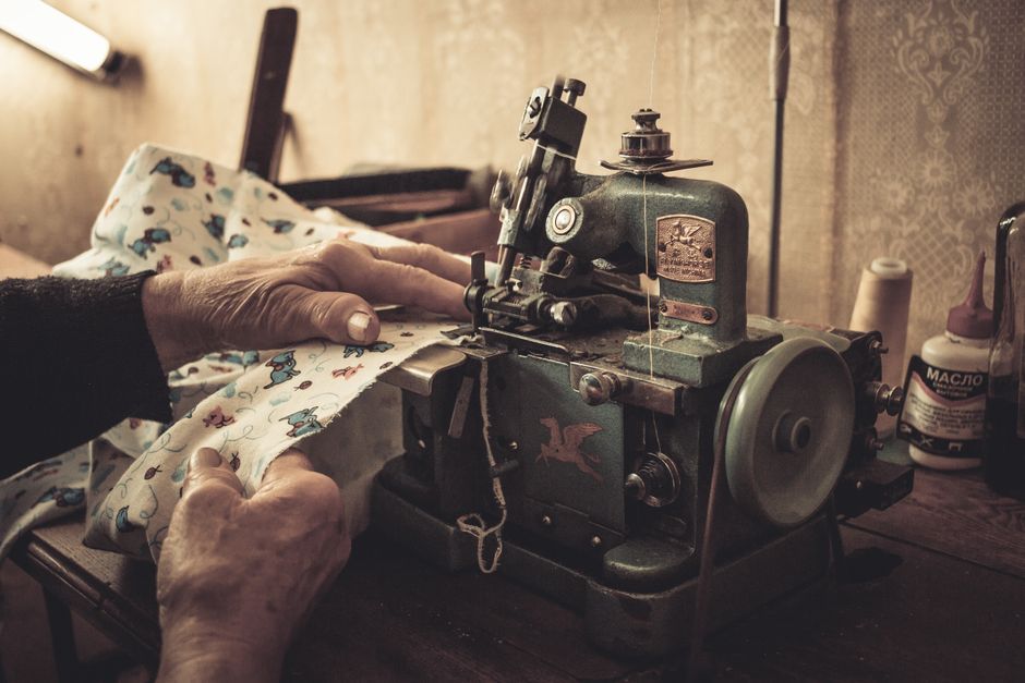 Close-up of a tailor's hands expertly stitching a seam on a garment, emphasizing the repair aspect of a wardrobe reset.