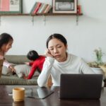 A parent with a tired but determined expression, holding a cup of coffee, looking at a messy kitchen table. Implies the struggle of getting back on track.