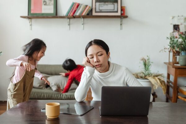 A parent with a tired but determined expression, holding a cup of coffee, looking at a messy kitchen table. Implies the struggle of getting back on track.