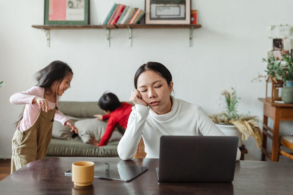 A parent with a tired but determined expression, holding a cup of coffee, looking at a messy kitchen table. Implies the struggle of getting back on track.