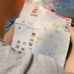 A person holding a city map, pointing to landmarks, with a blurred city skyline in the background, symbolizing travel planning for city passes and museum cards.