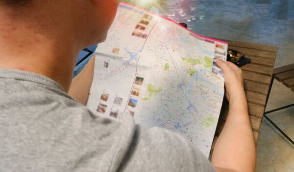 A person holding a city map, pointing to landmarks, with a blurred city skyline in the background, symbolizing travel planning for city passes and museum cards.