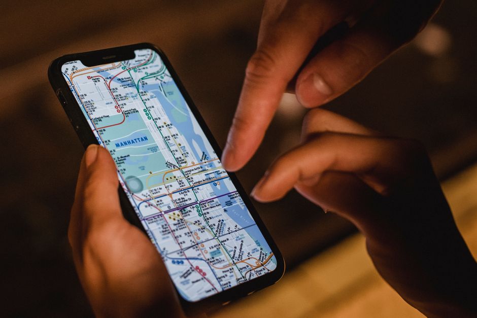 A traveler holding a smartphone displaying a public transport map, navigating their route in an urban setting.