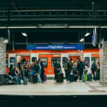 Travelers waiting for an airport express train at a modern, well-lit platform with luggage.