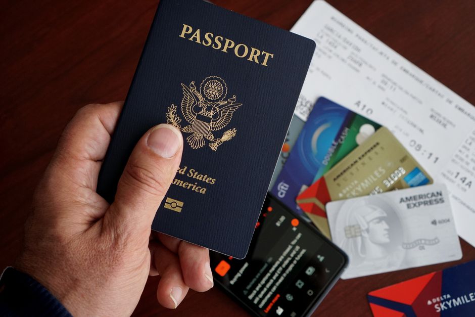 Overhead shot of a meticulously organized table with a passport, various currencies, a smartphone displaying travel apps, and a physical travel checklist.