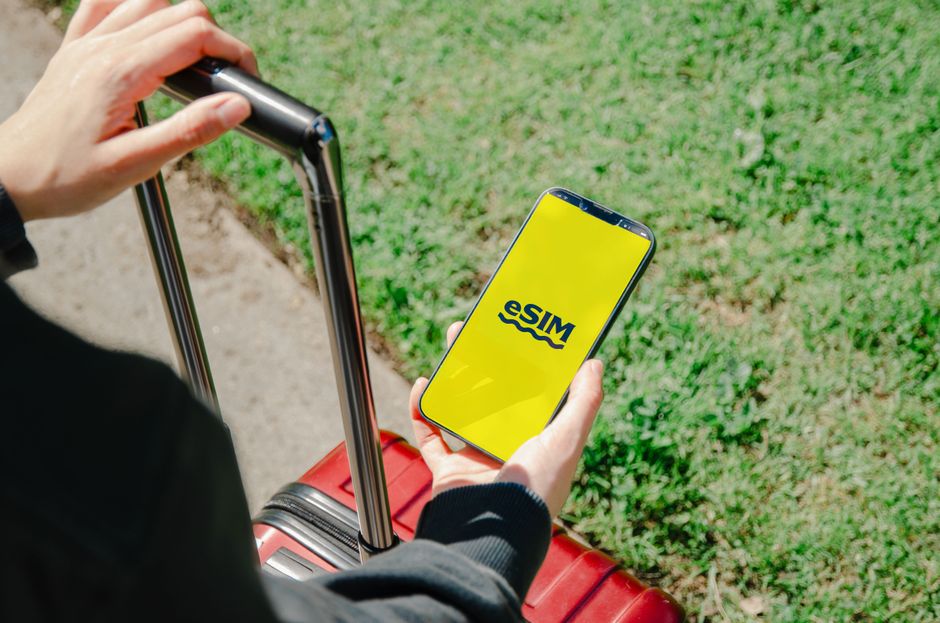 A smartphone screen displaying a detailed travel itinerary from an app like TripIt, with flight information and hotel bookings visible, held against a blurred airport background.