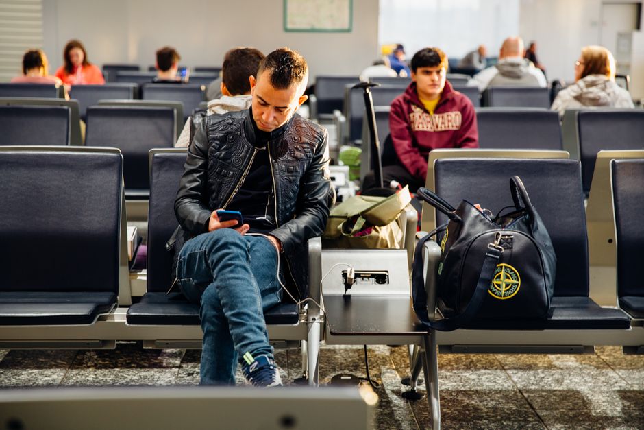 Traveler on a train charging a phone and tablet simultaneously with a portable power bank via USB-C cables.