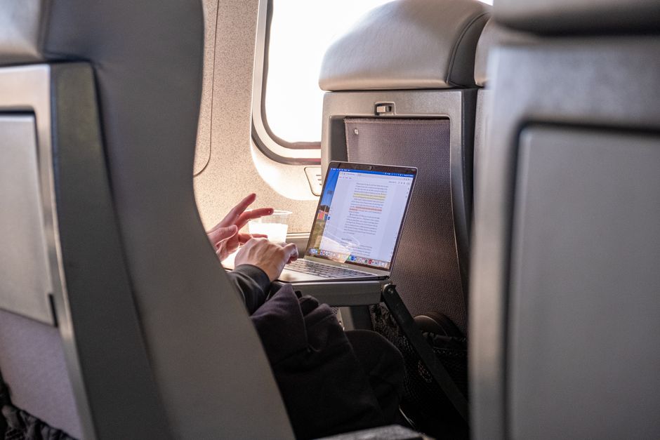 Close-up of hands typing on a laptop, comparing flight details and prices on a travel website.