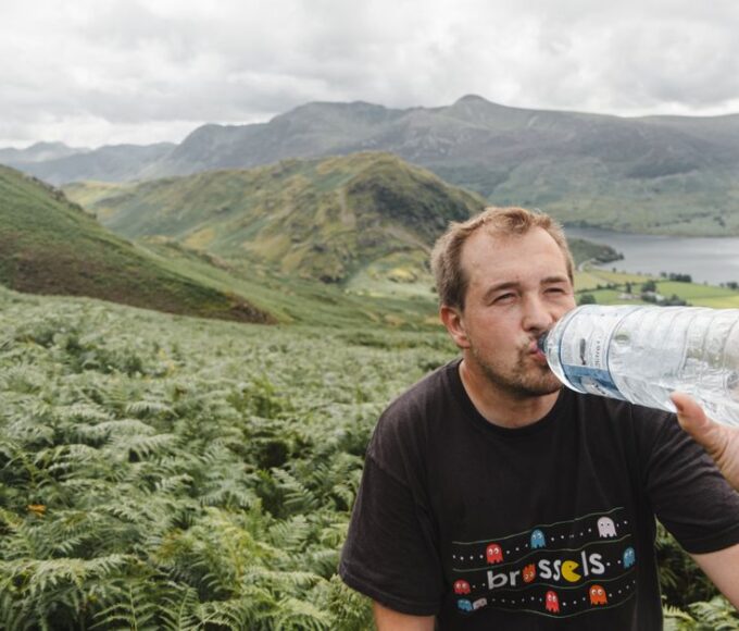 A person hydrating with a water bottle while looking out at a vast, sunny landscape, emphasizing the importance of staying hydrated during travel.