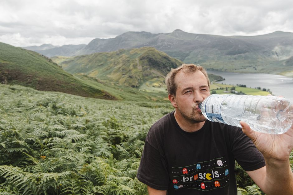 A person hydrating with a water bottle while looking out at a vast, sunny landscape, emphasizing the importance of staying hydrated during travel.