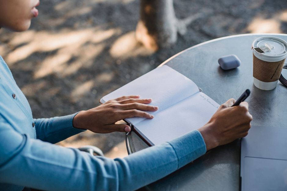 A solo traveler writes in a journal with a pen, next to a map and a cup of tea, planning their next steps calmly.