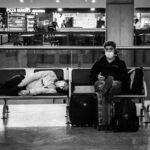 A tired traveler in a brightly lit airport terminal, clutching a carry-on, looking disoriented.