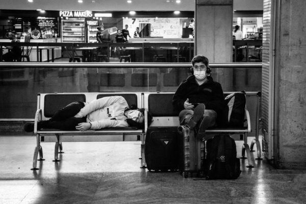 A tired traveler in a brightly lit airport terminal, clutching a carry-on, looking disoriented.