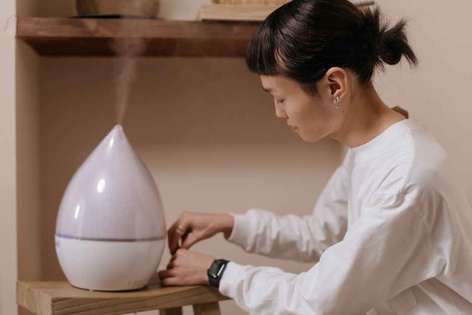 A compact portable humidifier emitting a fine mist on a hotel room nightstand, next to a person's hand reaching for it, emphasizing humidification for vocal protection.