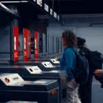 A person from North America, possibly a solo traveler, validating a train ticket at a yellow machine on a European train platform, avoiding a common mistake.