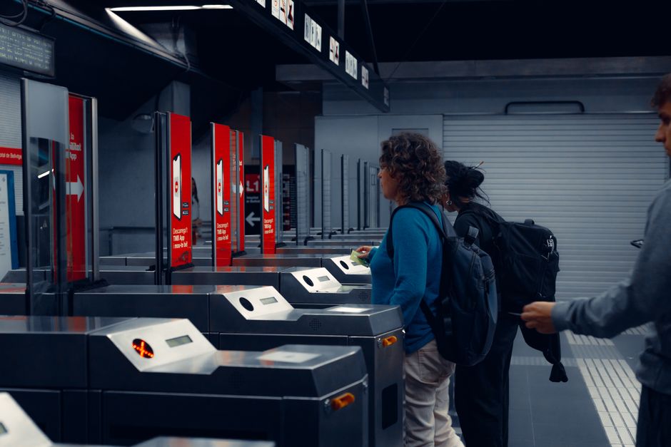 A person from North America, possibly a solo traveler, validating a train ticket at a yellow machine on a European train platform, avoiding a common mistake.