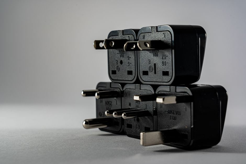A universal travel adapter plugged into a foreign wall socket with USB cables connected, ready to charge devices.