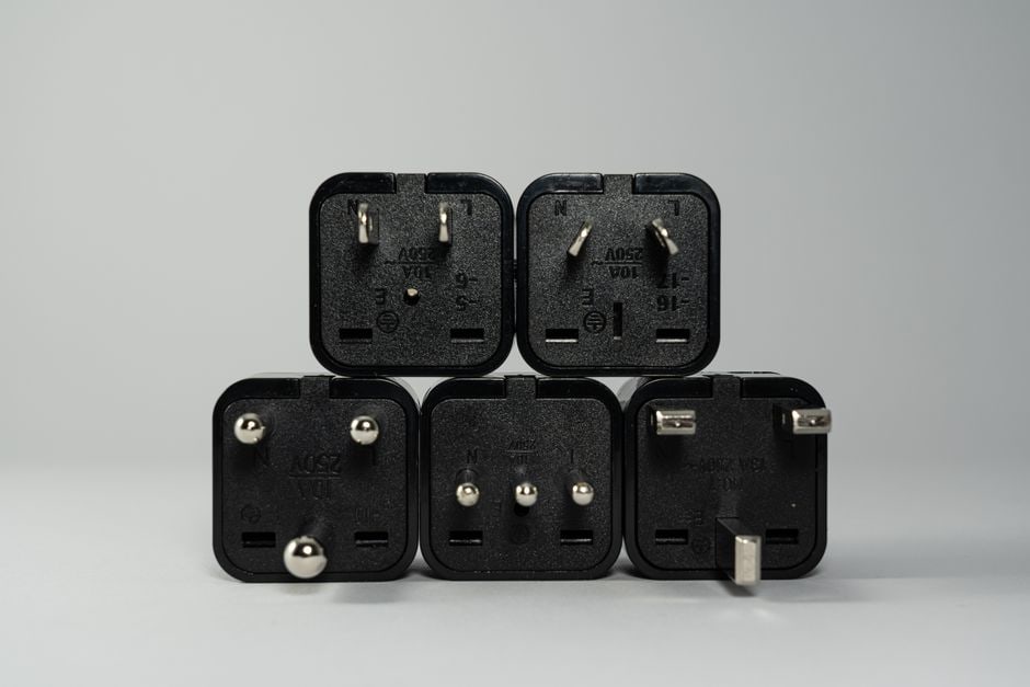 A close-up shot of a universal travel adapter displaying various interchangeable international plugs (European, North American) with multiple USB-C and USB-A ports.