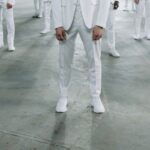 A pair of pristine white leather sneakers styled with grey tailored trousers and a light blue shirt, suitable for a business casual environment.