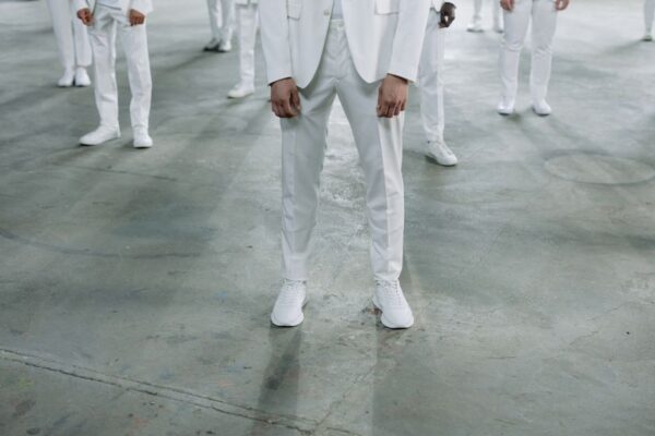 A pair of pristine white leather sneakers styled with grey tailored trousers and a light blue shirt, suitable for a business casual environment.